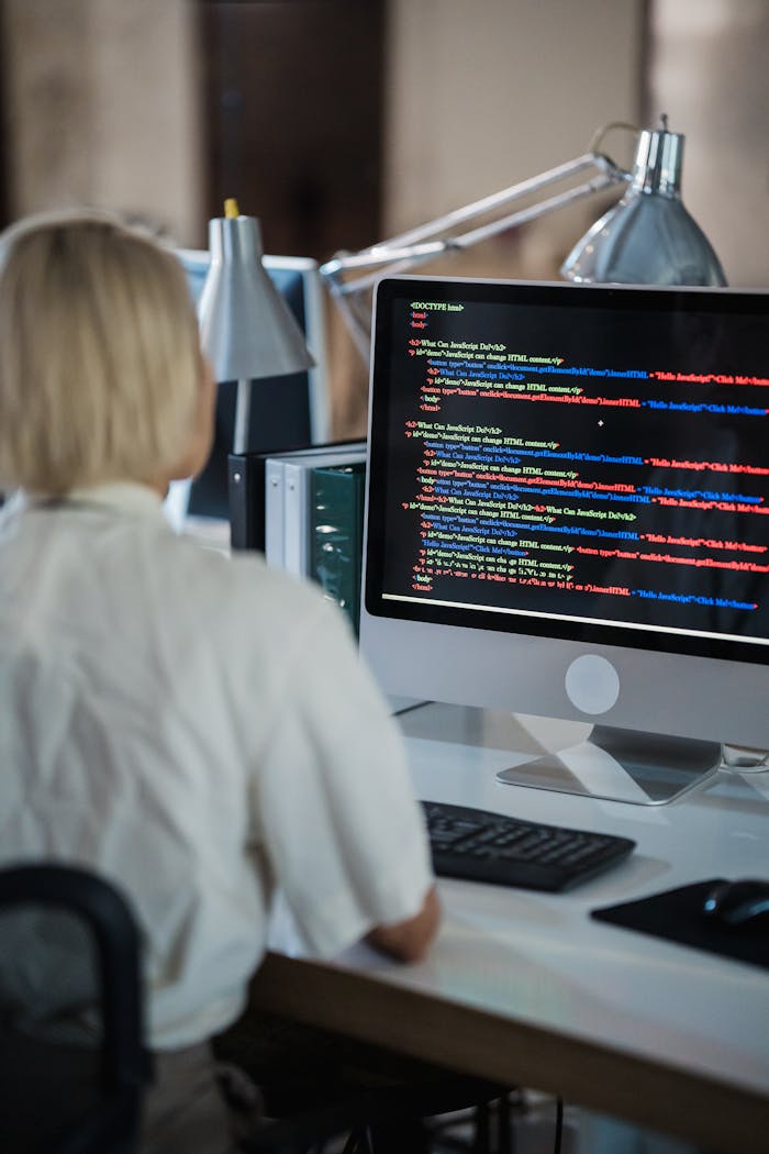 contact-img Professional woman coding at office desk with two monitors and desk lamps.